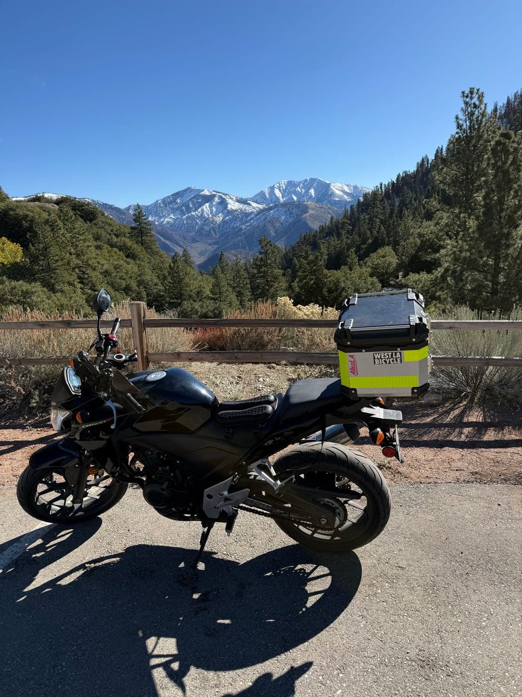 A black Honda CB500F with a top case at a mountain pullout, snow on the peaks behind